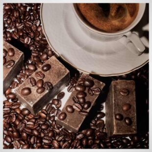 Mydlo kawowe Savon Cosmetics krojone ręcznie na tle filiżanki kawy posypane ziarnami kawy